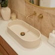 Modern bathroom vanity with oval sink, gold faucet, and beige tiled wall.
