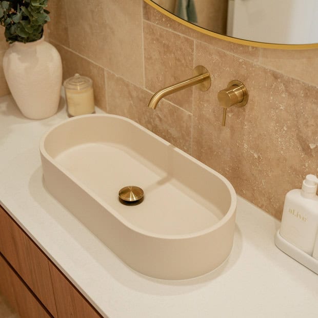 Modern bathroom vanity with oval sink, gold faucet, and beige tiled wall.