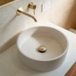 Stylish round white bathroom basin with gold faucet and drain, modern design.
